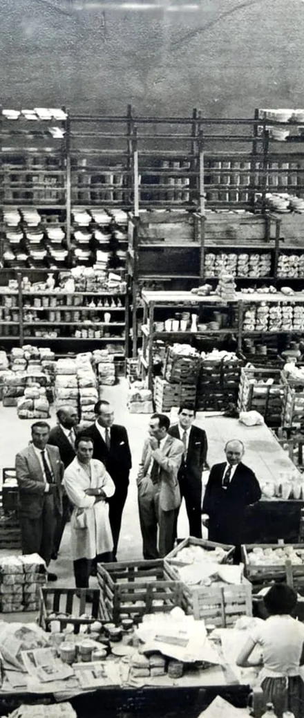 Fotografia histórica de trabalhadores em uma fábrica de porcelana com prateleiras cheias de peças
