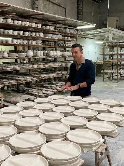 Rogério Teixeira ao lado de pratos de porcelana em produção na fábrica.