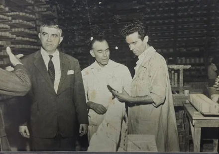 Fotografia histórica de Zezito conversando com dois homens em avental sobre uma peça de porcelana